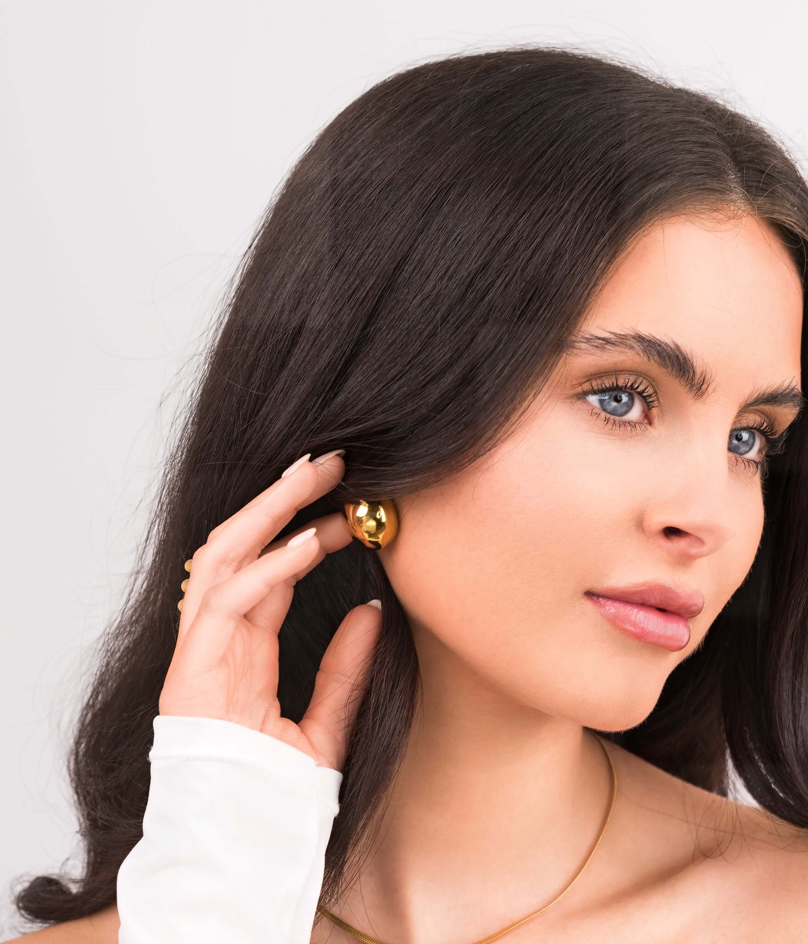 Model wearing ARIIRA Sana Gold Sculpted Dome Earrings, showcasing elegant gold-plated studs with a modern silhouette.