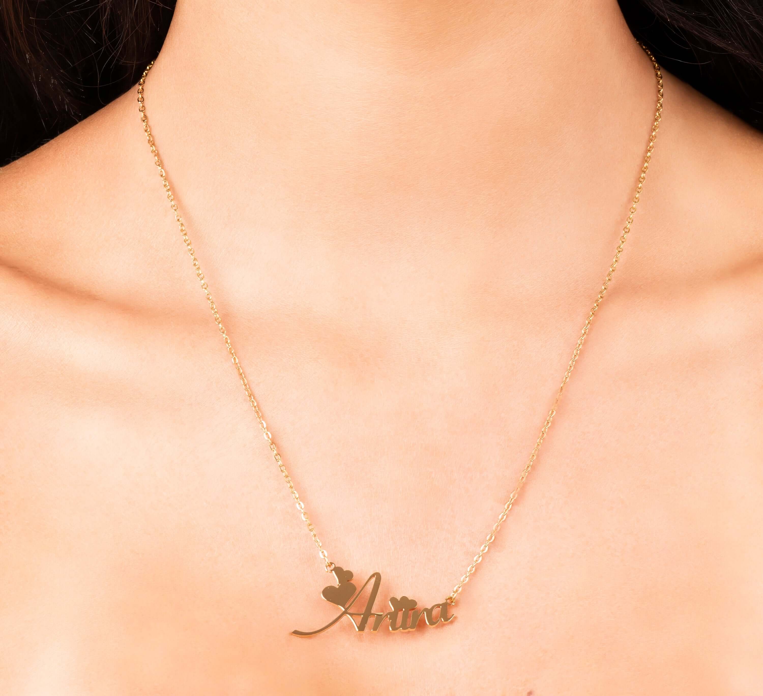 Gold Amira custom name necklace featuring flowing script and heart details, worn elegantly on a model's neck.