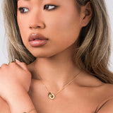 Model showcasing Reina Roman Circle Pendant Necklace with crystal charm and layered bracelet, elegant and timeless jewelry.