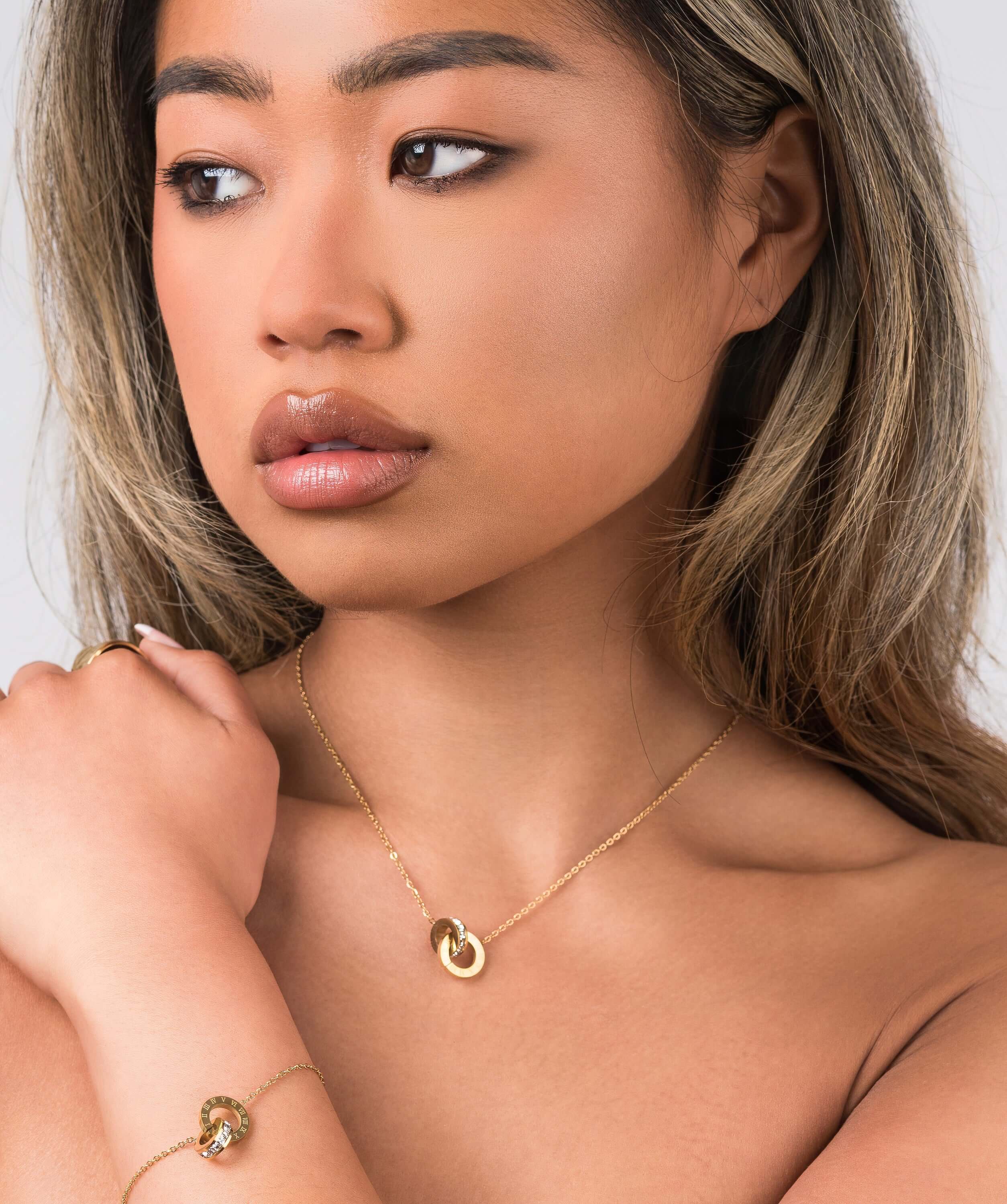 Model showcasing Reina Roman Circle Pendant Necklace with crystal charm and layered bracelet, elegant and timeless jewelry.