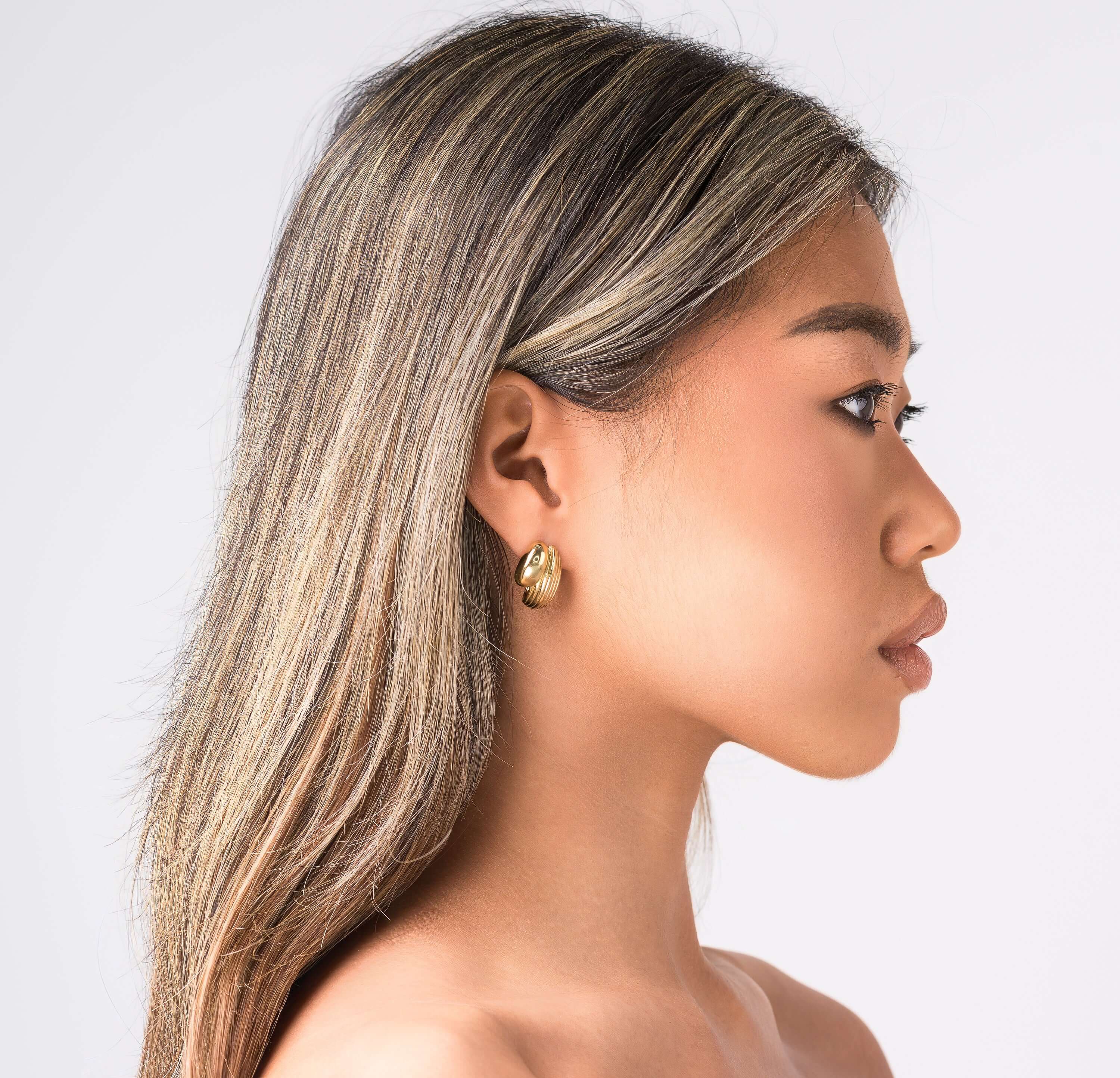 Profile view of a model wearing ARIIRA textured curve hoop earrings, showcasing elegance and modern design.