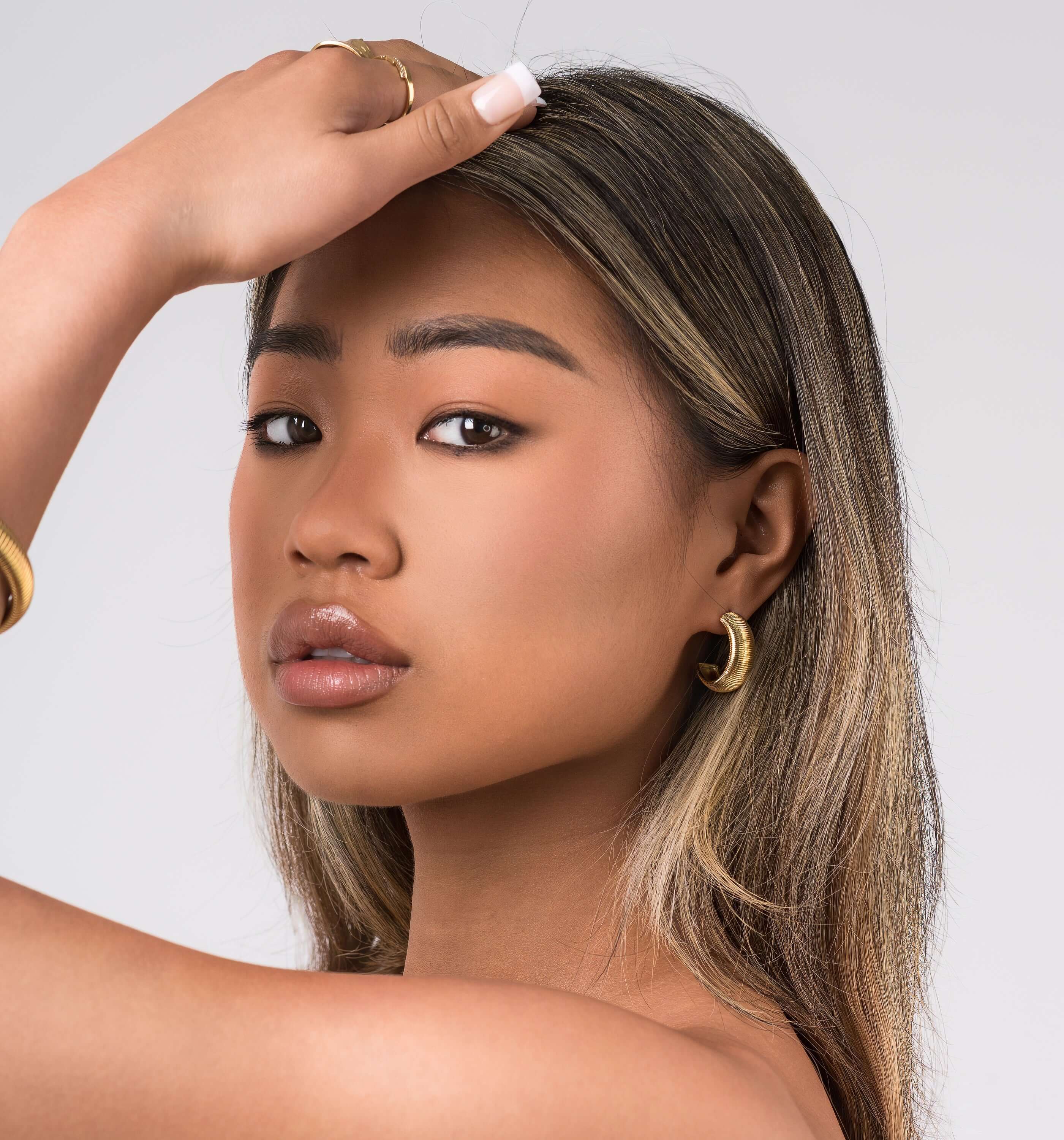 Young woman showcasing Selene Ribbed Hoop Earrings, featuring fine ridged detailing and a polished brushed finish.