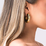 Close-up of a model wearing ARIIRA Rhea Sculpted Dome Hoop Earrings in polished gold.