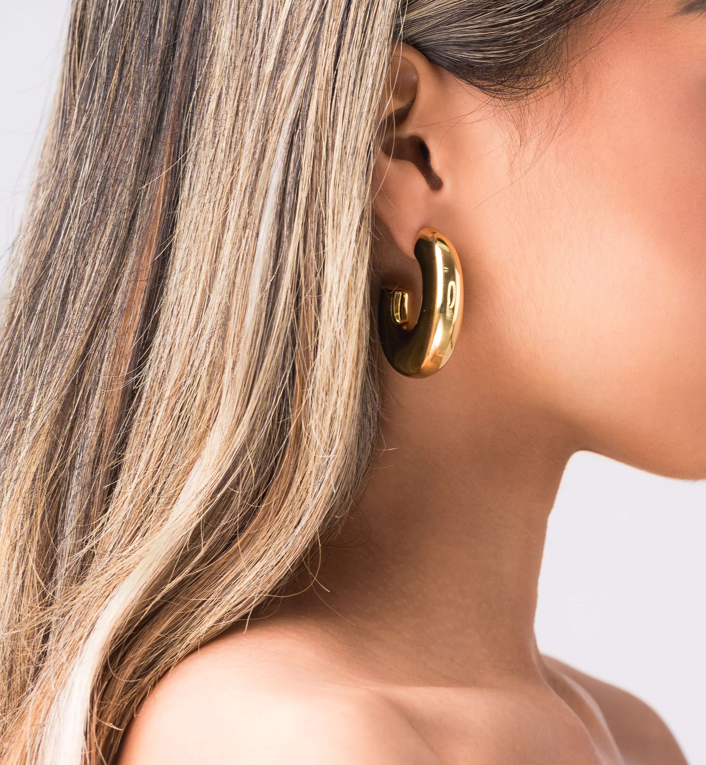 Close-up of a model wearing ARIIRA Rhea Sculpted Dome Hoop Earrings in polished gold.