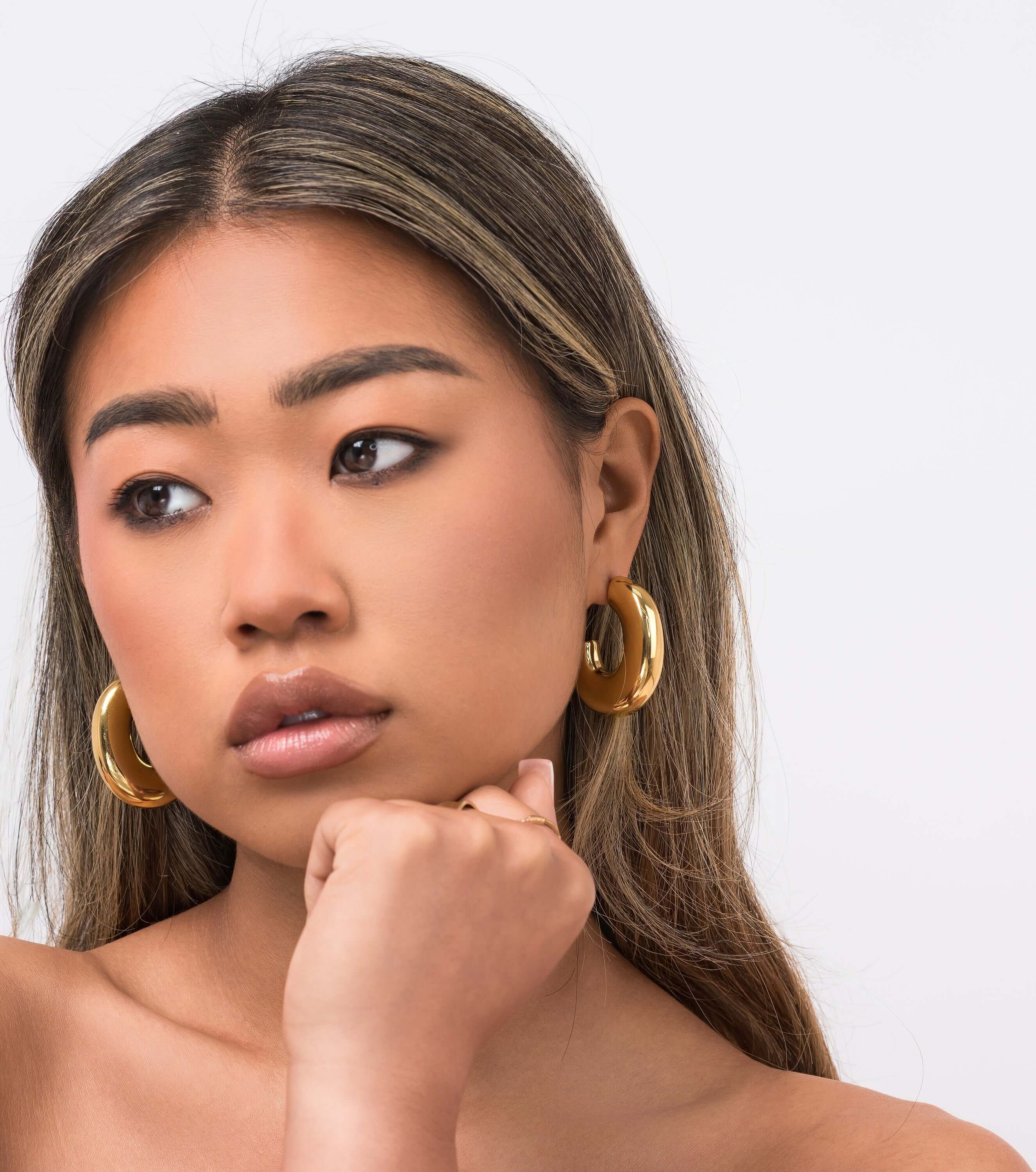 Stylish woman wearing ARIIRA Rhea Sculpted Dome Hoop Earrings, showcasing modern elegance in gold.