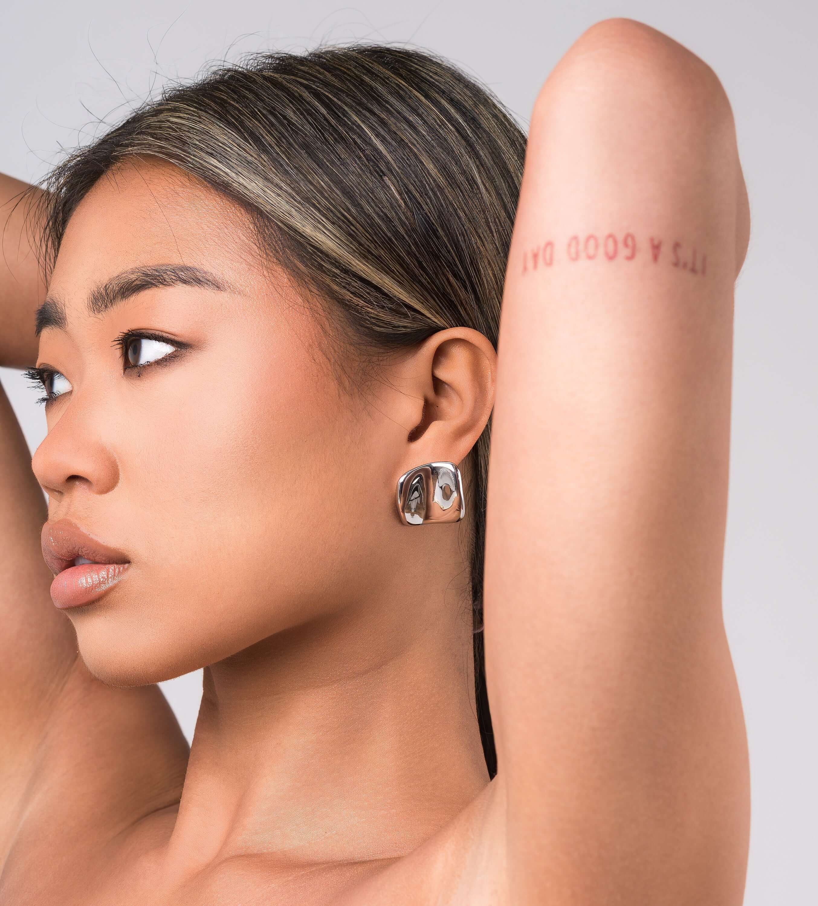 A model showcasing ARIIRA's Lara Organic Drop Studs earrings, highlighting their modern design and polished finish.