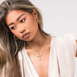 Model wearing ARIIRA Yasira Crystal Cross Pendant Necklace with elegant gold hoop earrings.