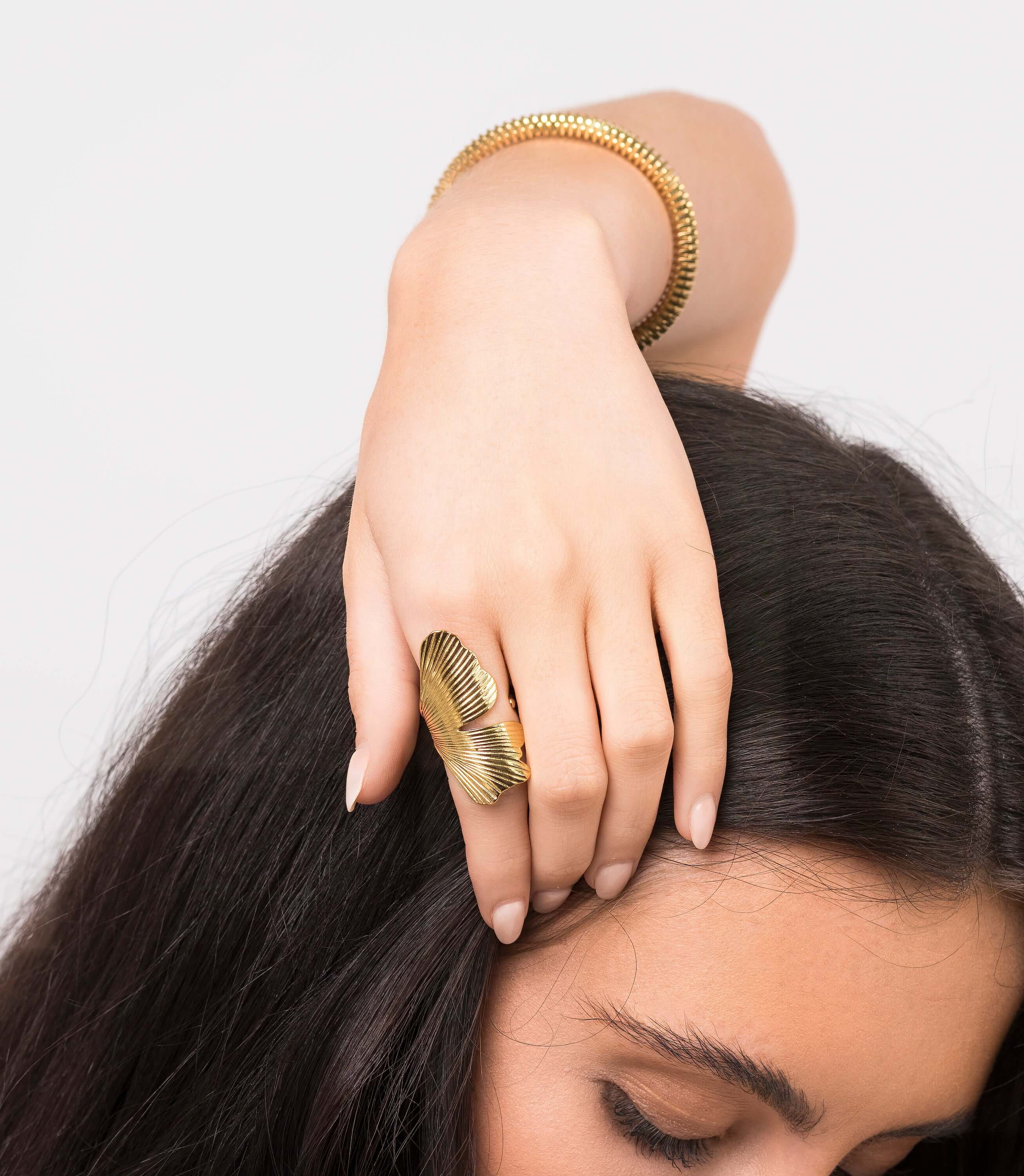 Woman wearing the ARIIRA Aria Winged Textured Adjustable Ring and a gold bracelet, showcasing elegance and style.
