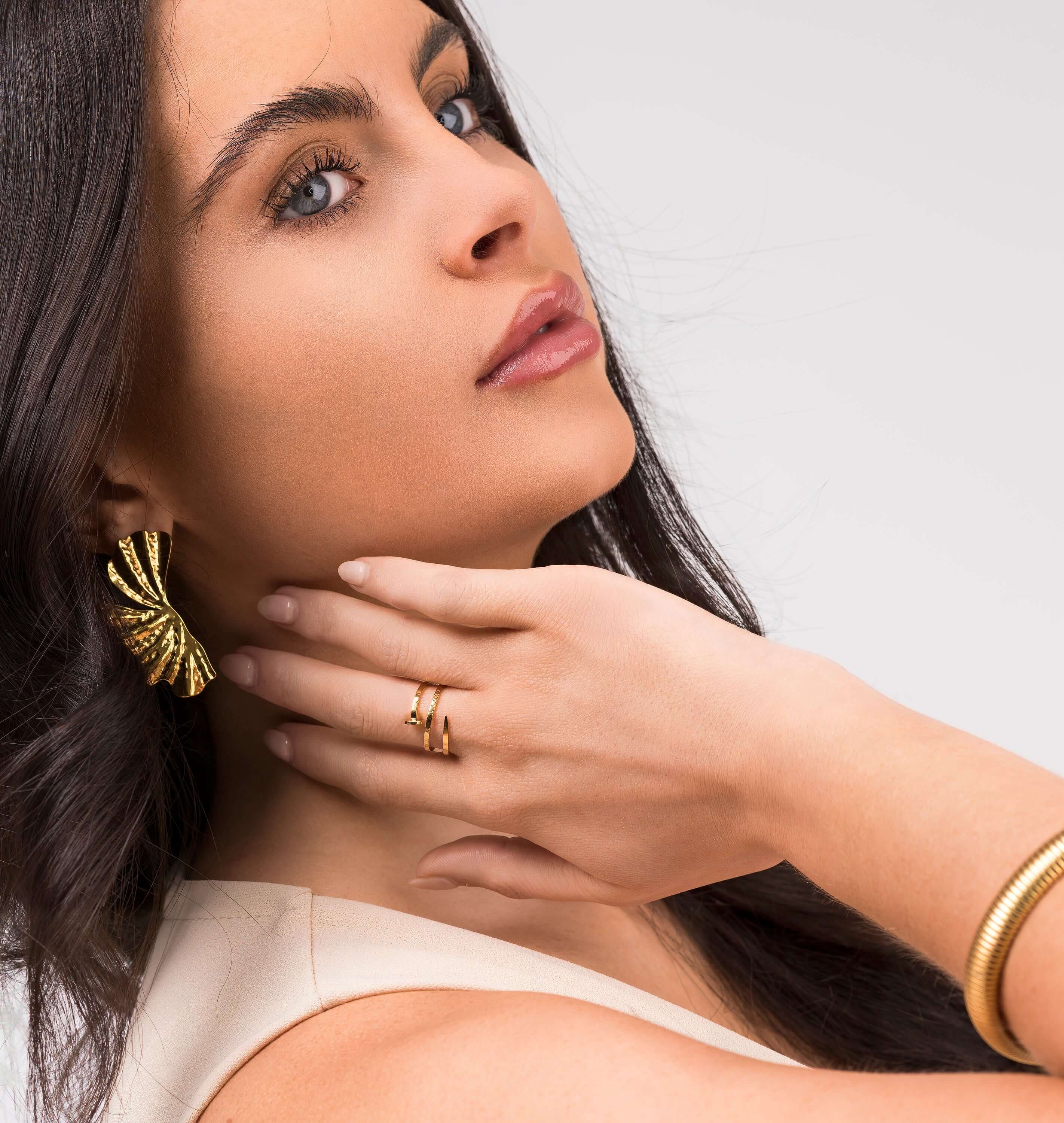 Model showcasing Zehra Textured Spiral Wrap Ring and bold gold earrings from ARIIRA, emphasizing modern women's jewelry.