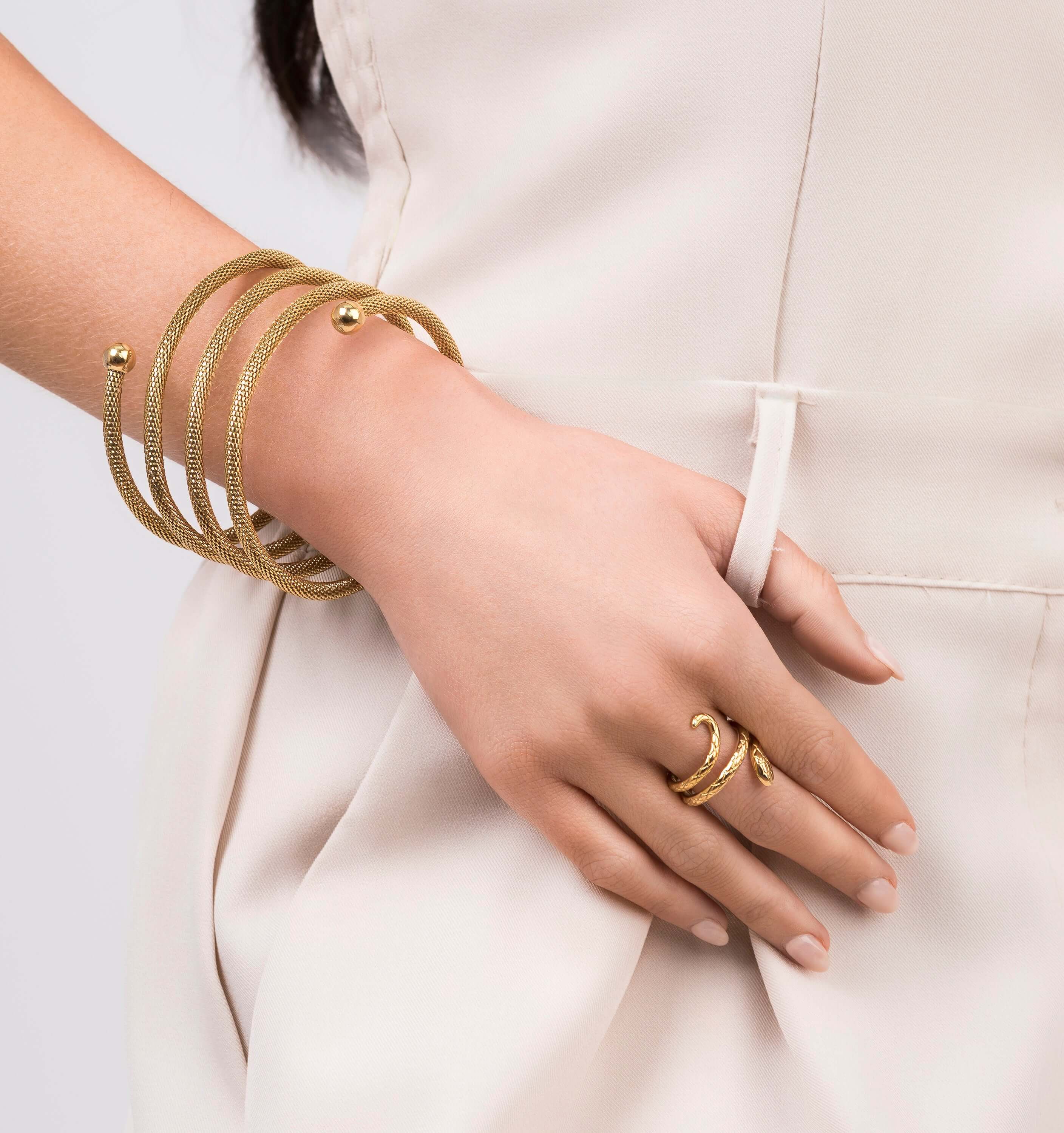 Zina Spiral Mesh Coil Bracelet by ARIIRA worn on wrist, showcasing a flexible gold design with polished end spheres.