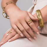 Close-up of hands wearing Mira Twin Band Floral Open Ring from ARIIRA, showcasing gold jewelry with floral motifs.
