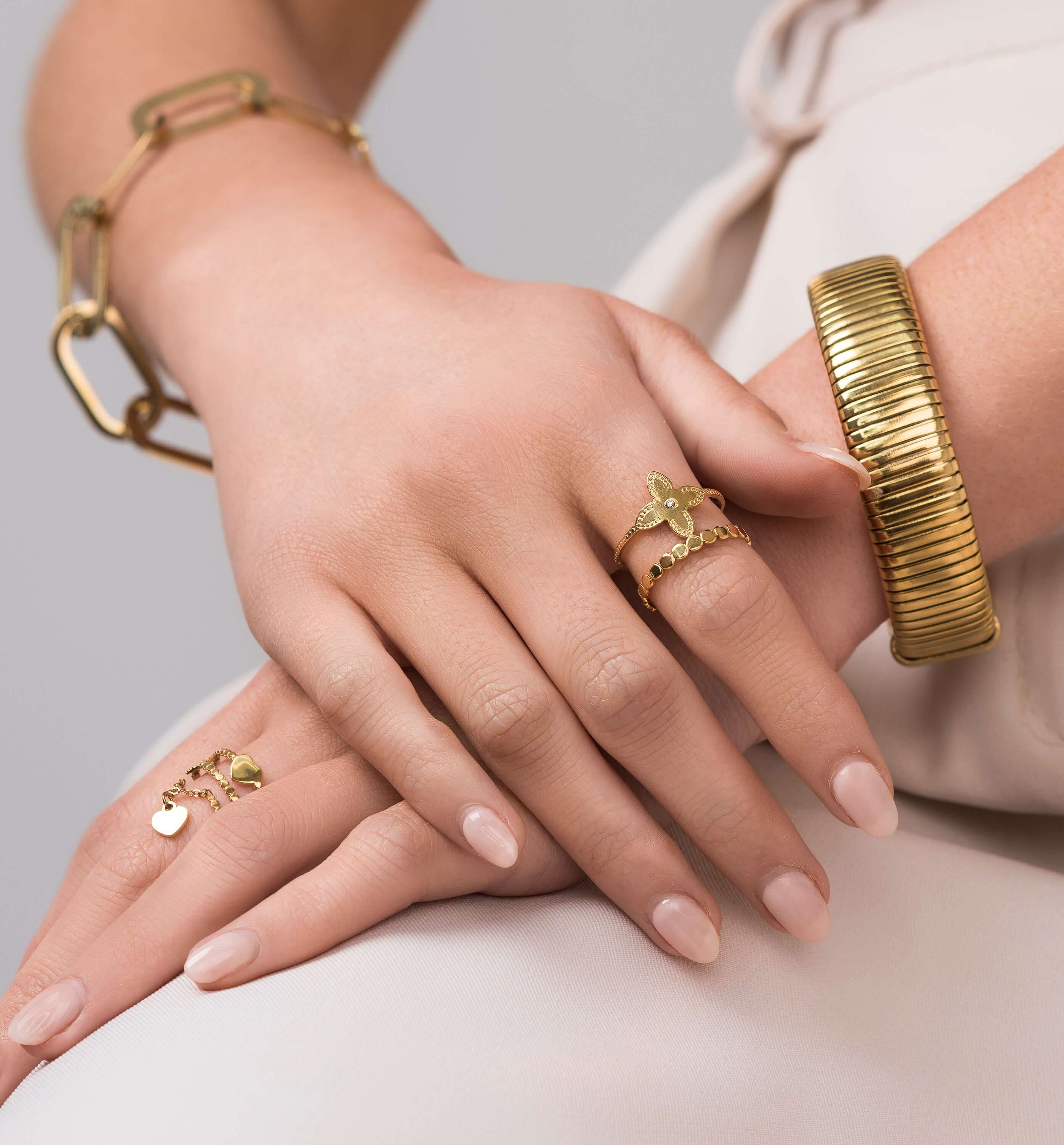 Close-up of hands wearing Mira Twin Band Floral Open Ring from ARIIRA, showcasing gold jewelry with floral motifs.