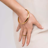 Close-up of a hand wearing ARIIRA's gold textured chain link ring and a sleek bangle on a light fabric background.