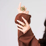 Woman wearing Naya Monstera Leaf Statement Ring and another gold ring, showcasing elegant jewelry against a neutral background.