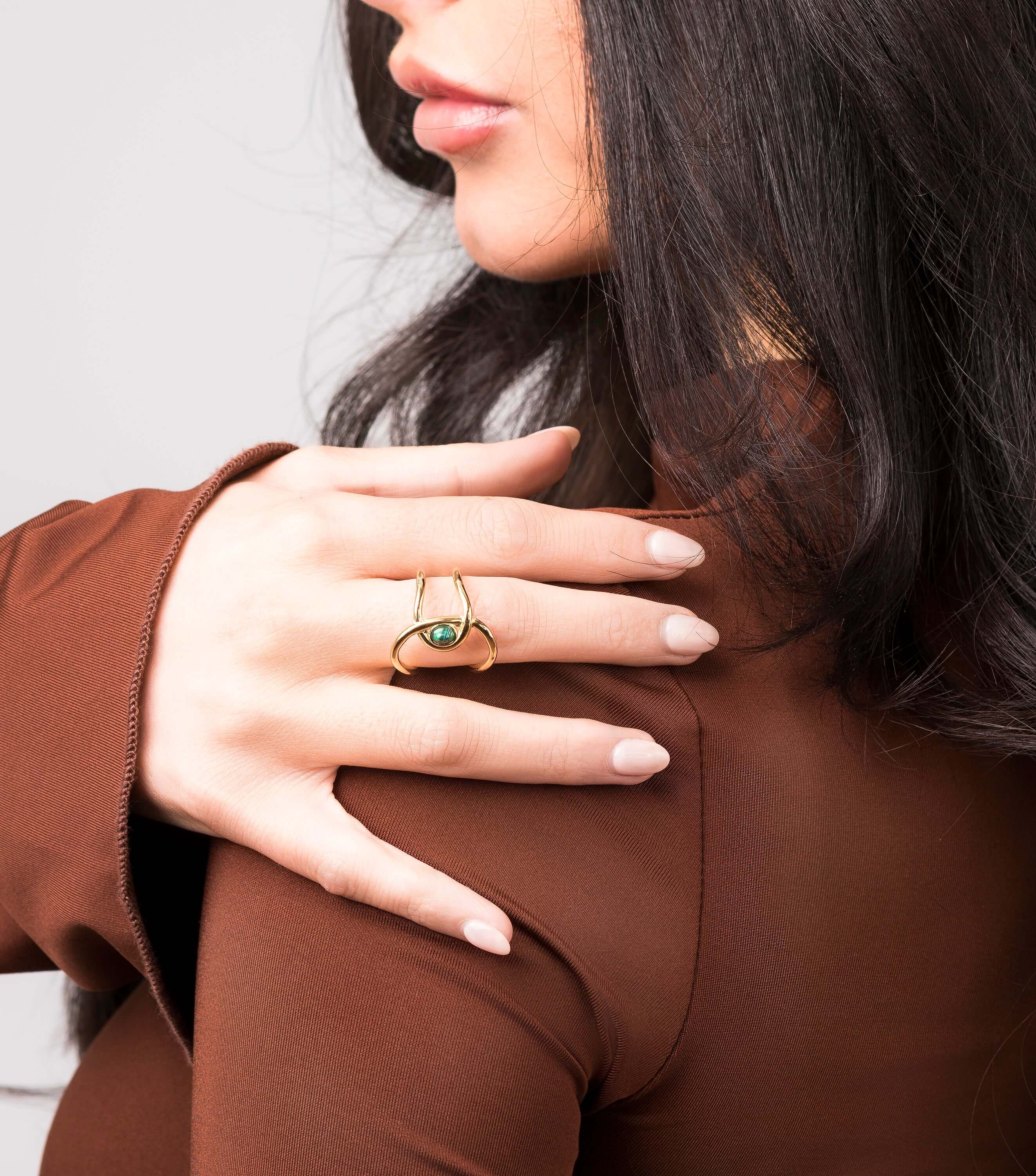 Close-up of a woman wearing an adjustable Lyra green stone open ring by ARIIRA, showcasing its modern gold design.