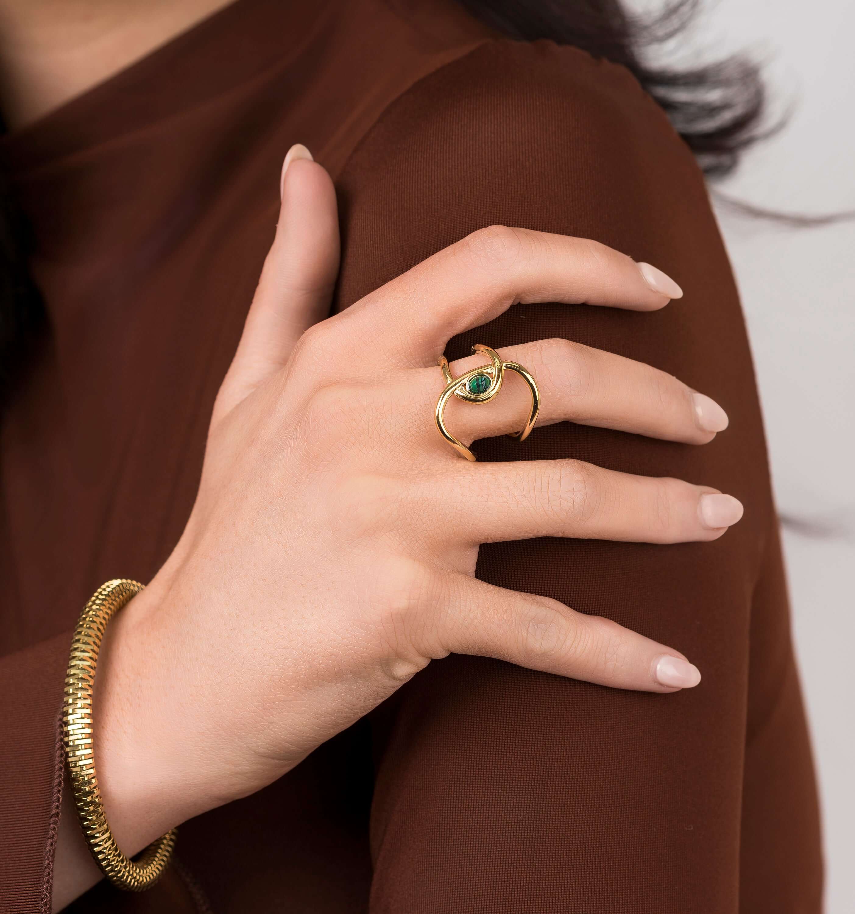 Close-up of a hand wearing the ARIIRA Lyra Green Stone Open Ring, featuring a gold design and deep green stone.