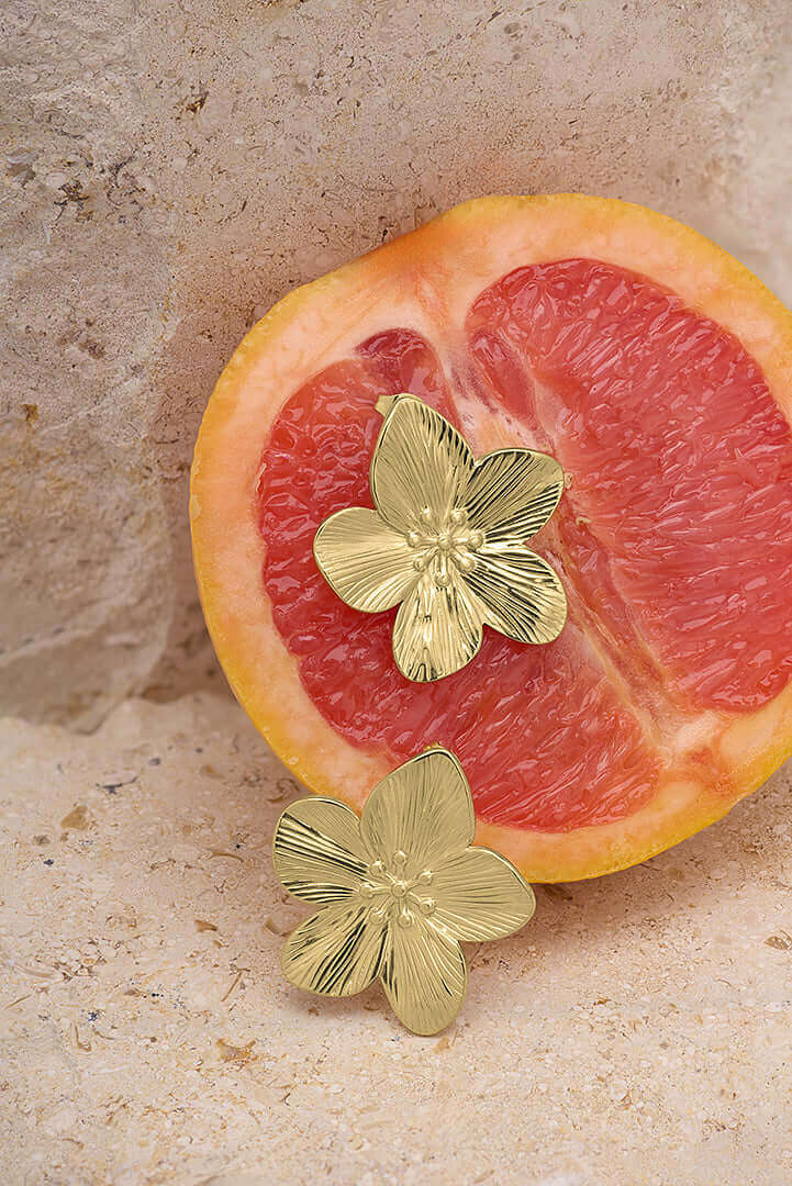 Elegant gold flower earrings placed on a sliced grapefruit, showcasing a unique citrus and jewelry combination.