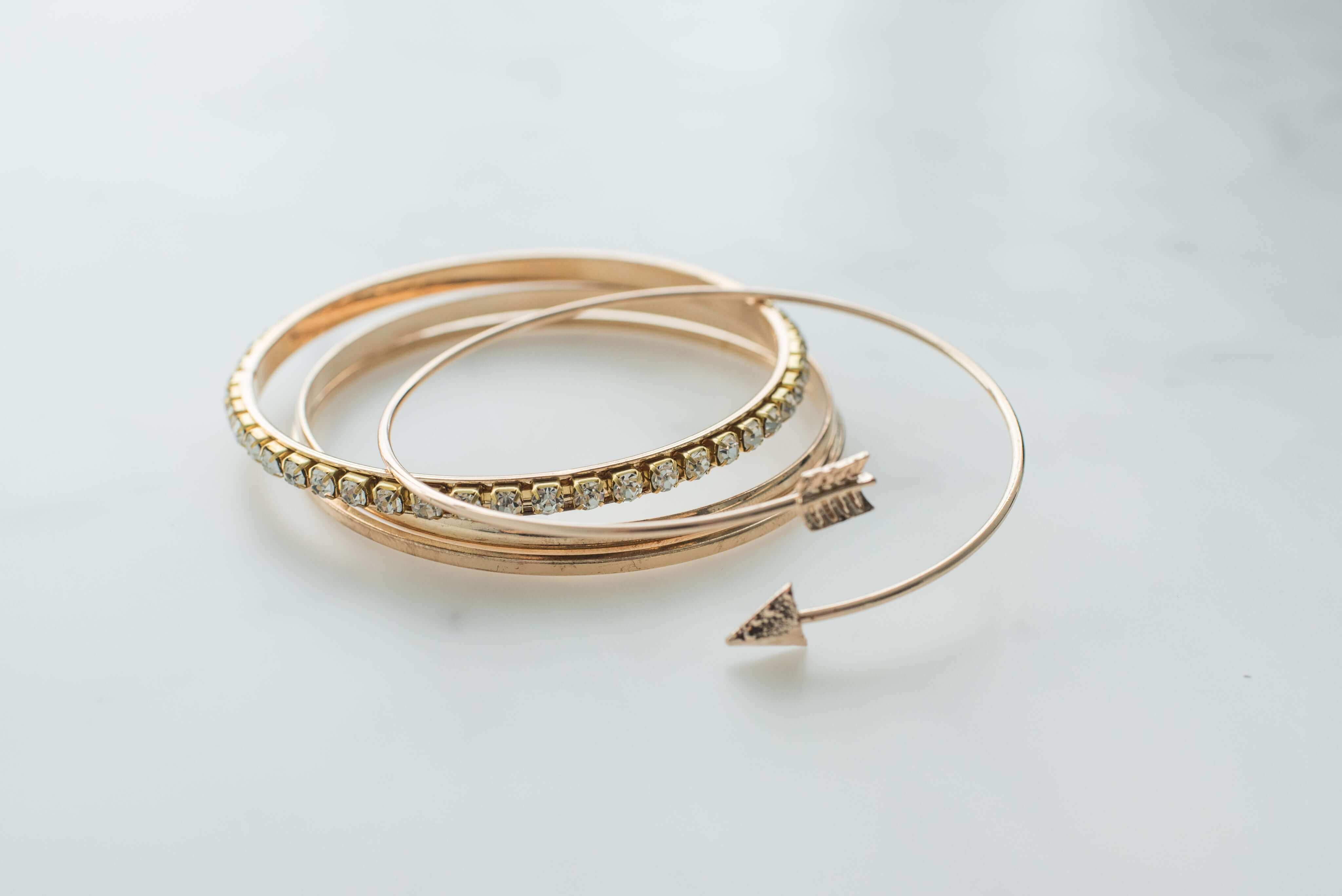 Gold bangles with sparkling gems and unique arrow design on a smooth marble surface.