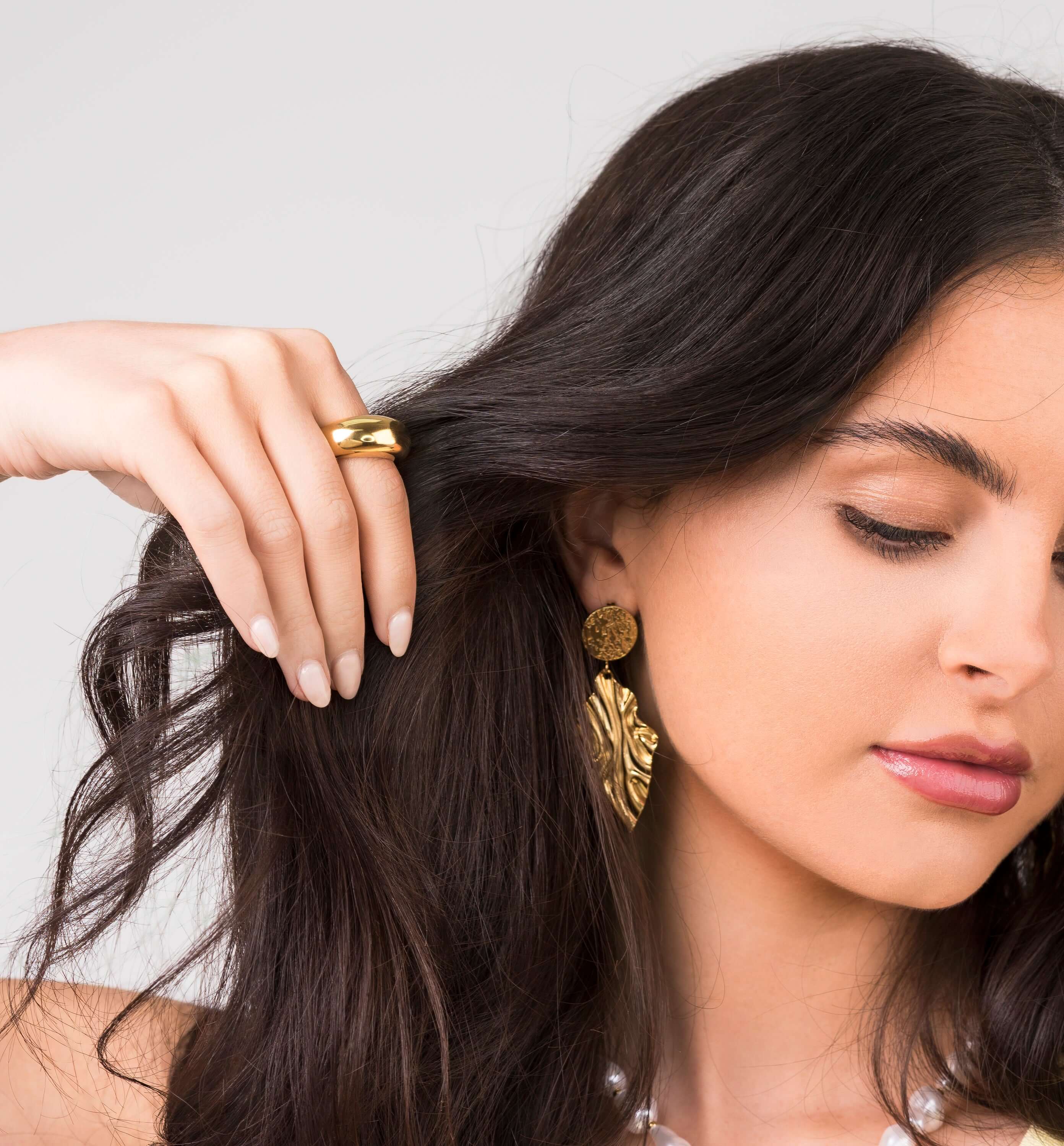 Close-up of a woman wearing the Noura Dome Band Ring and statement earrings, showcasing a stylish jewelry look.