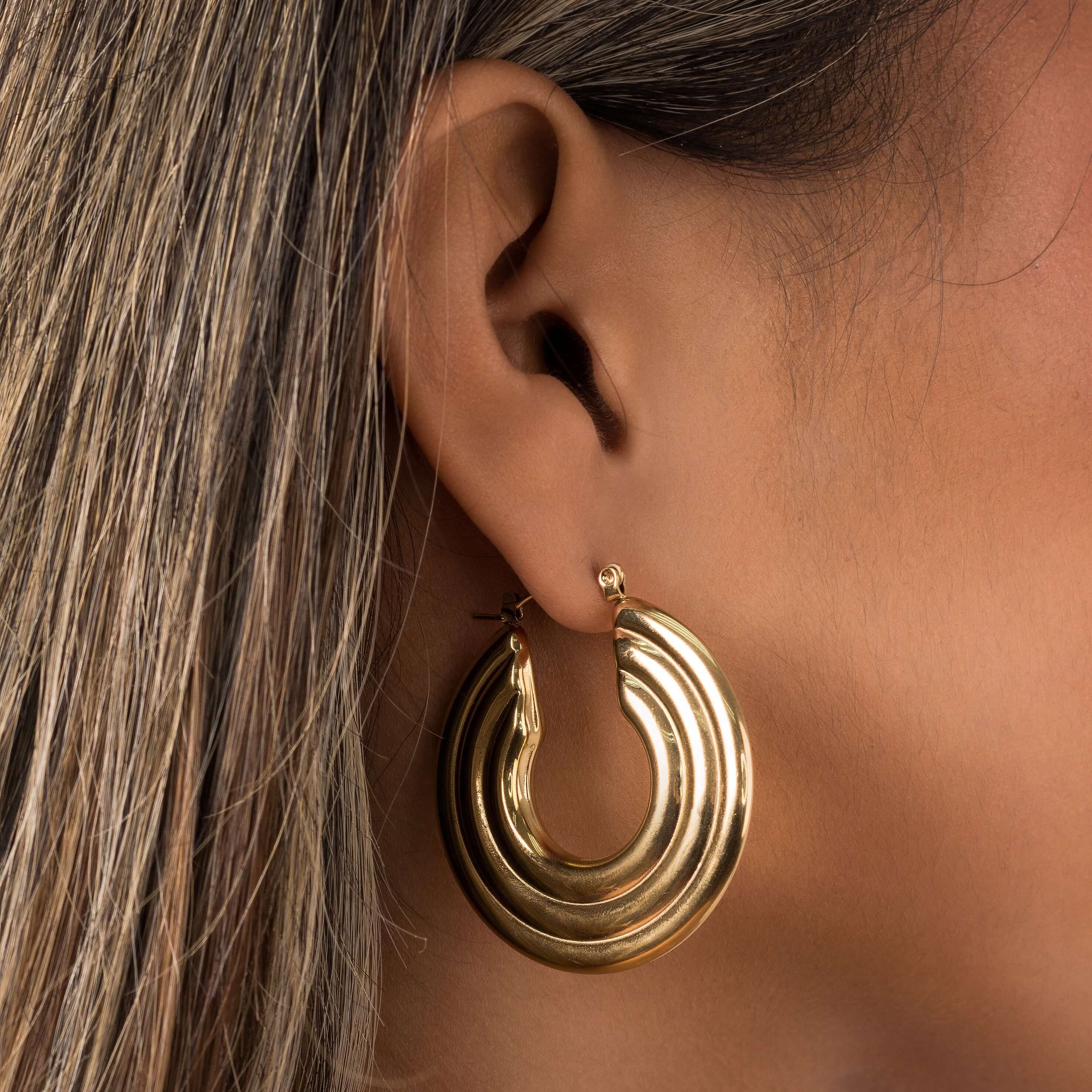 Stylish Elia Sculpted Oval Hoop Earrings in gold featuring ridged design, showcasing a close-up on an ear.