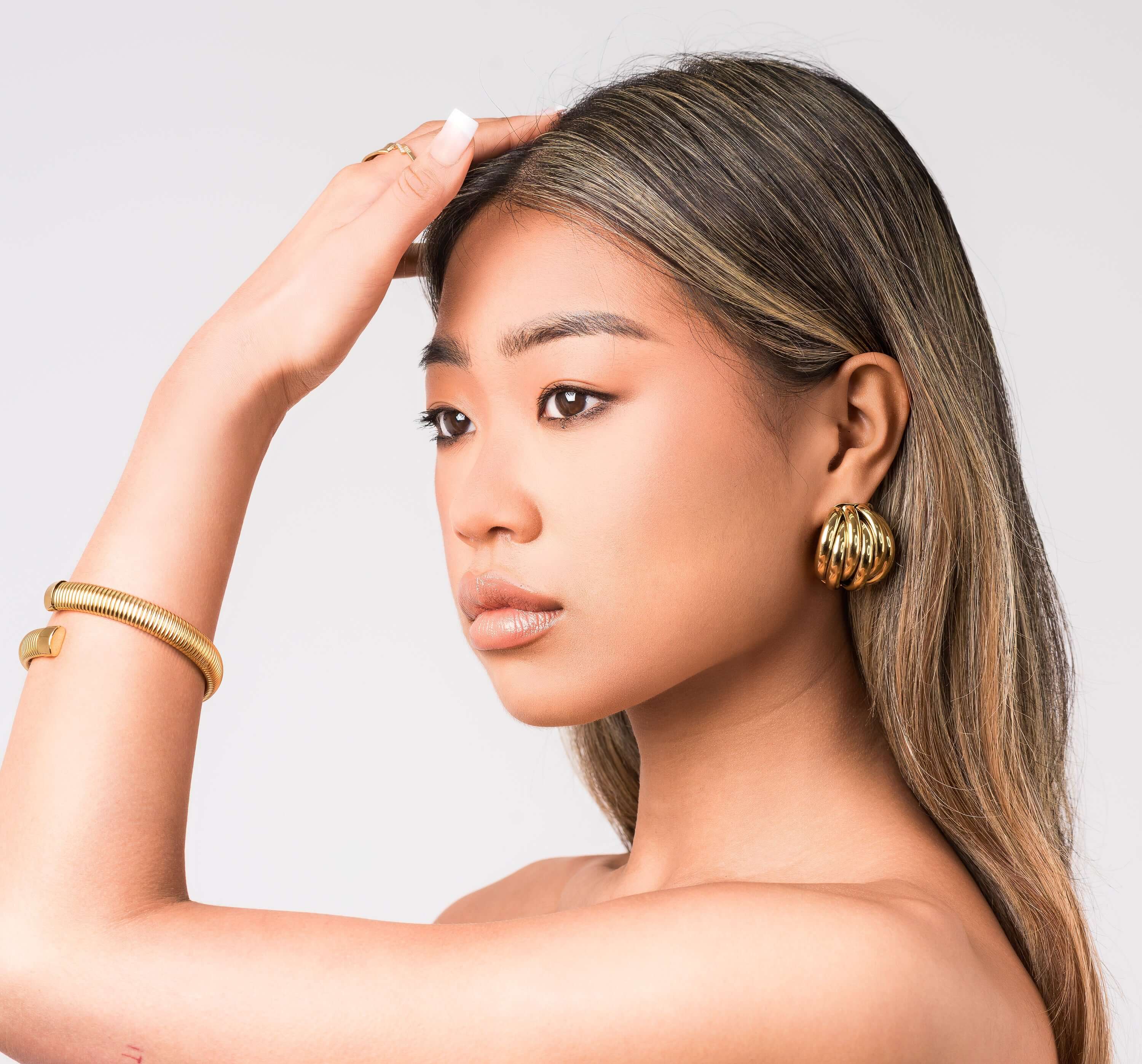 Model showcasing Yara Ribbed Dome Statement Earrings with a high-polish gold finish and a sleek hairstyle.