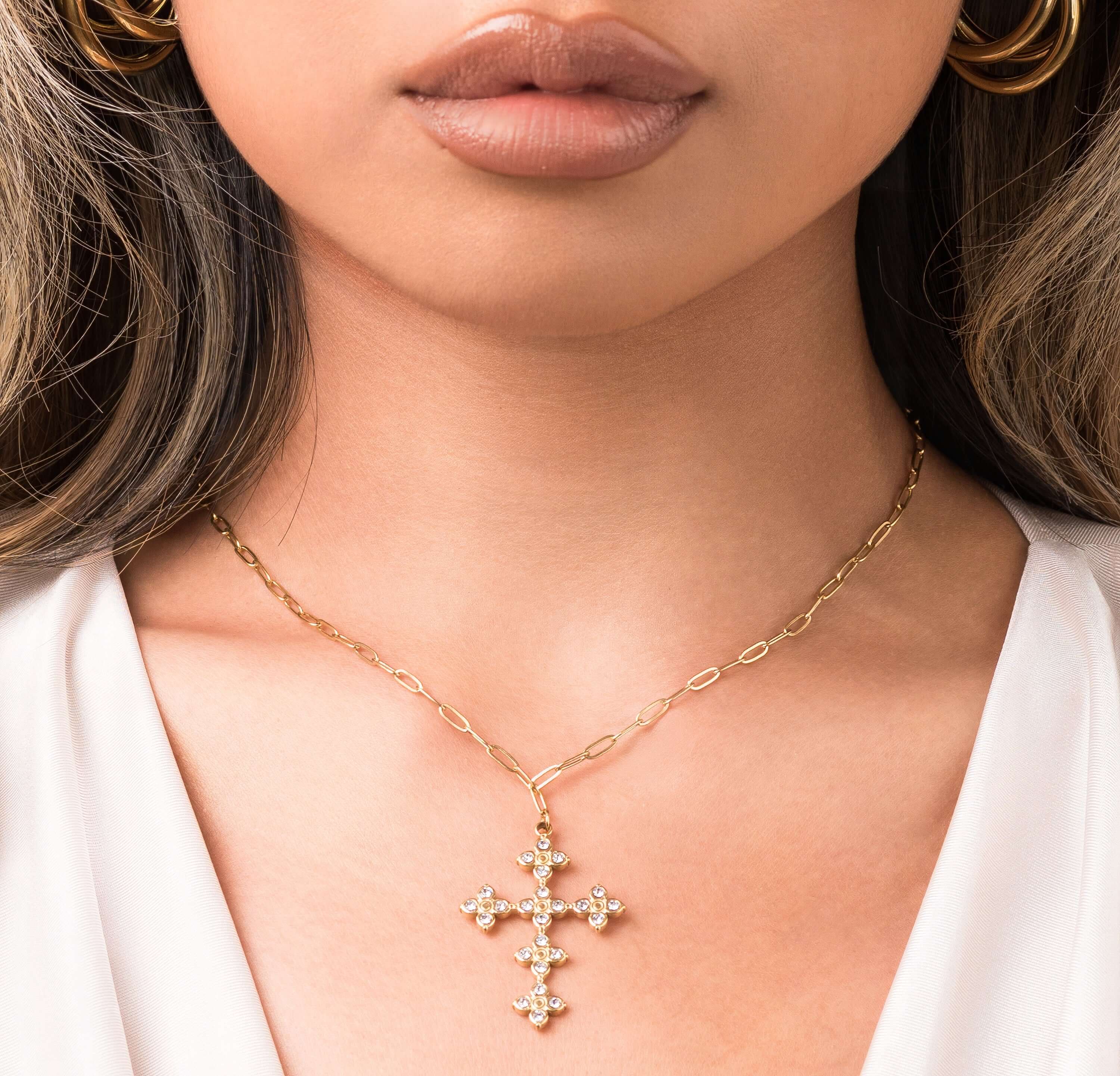 Close-up of a woman wearing the ARIIRA Crystal Cross Pendant Necklace with shimmering stones on a gold chain.