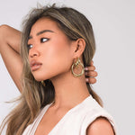 ARIIRA Alma Sculpted Knot Drop Earrings worn by a woman, showcasing bold design and polished shine.