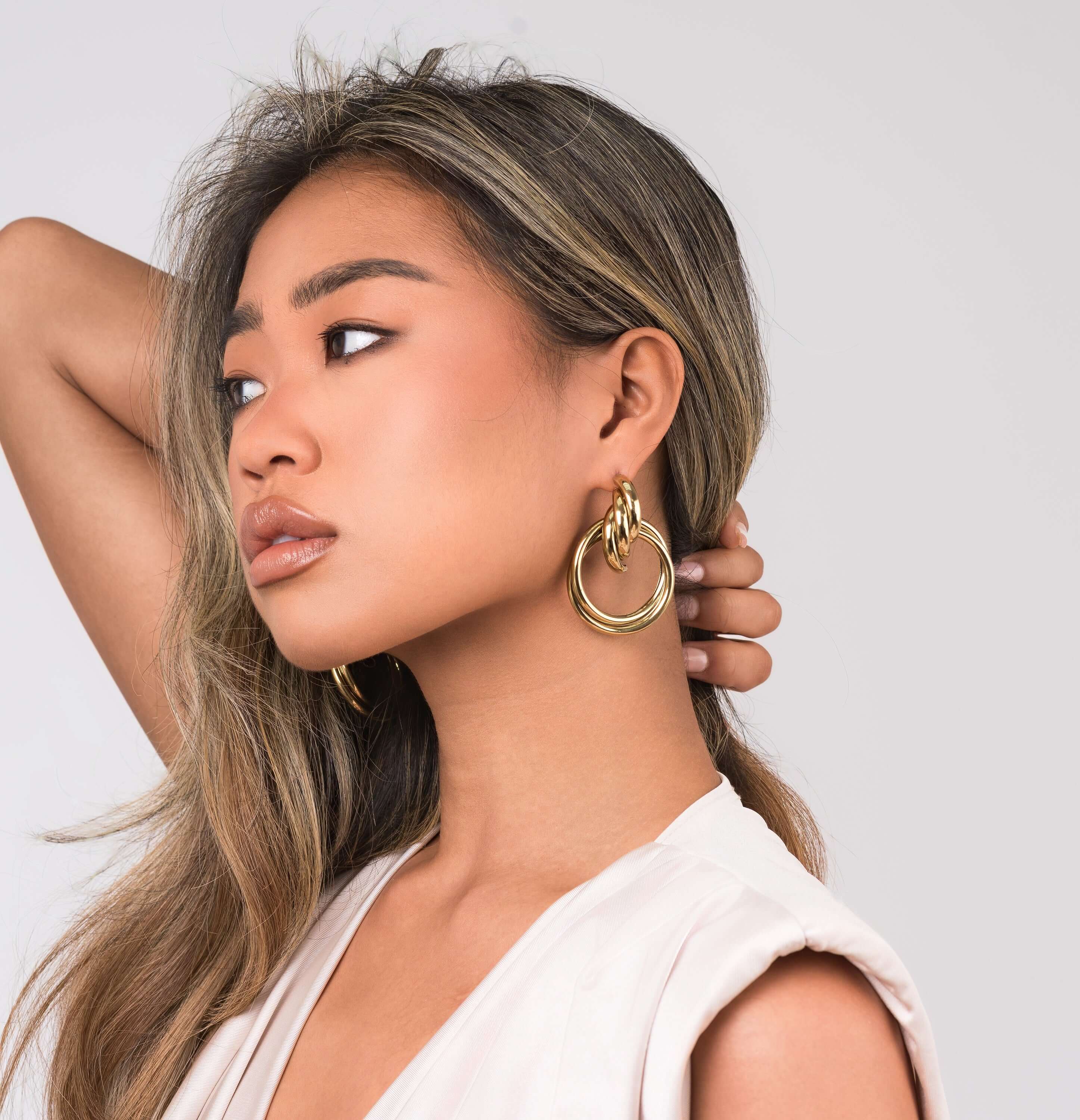 ARIIRA Alma Sculpted Knot Drop Earrings worn by a woman, showcasing bold design and polished shine.