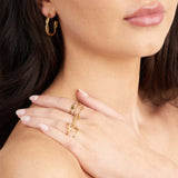 Close-up of a model wearing gold jewelry, featuring a Lyla Orbit Open Ring by ARIIRA and elegant hoop earrings.